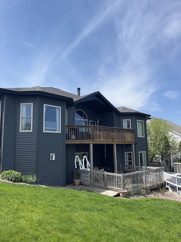 A modern home with dark siding and a wooden deck in a green yard
