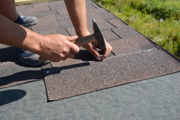 A worker is installing shingles on a roof using a hammer