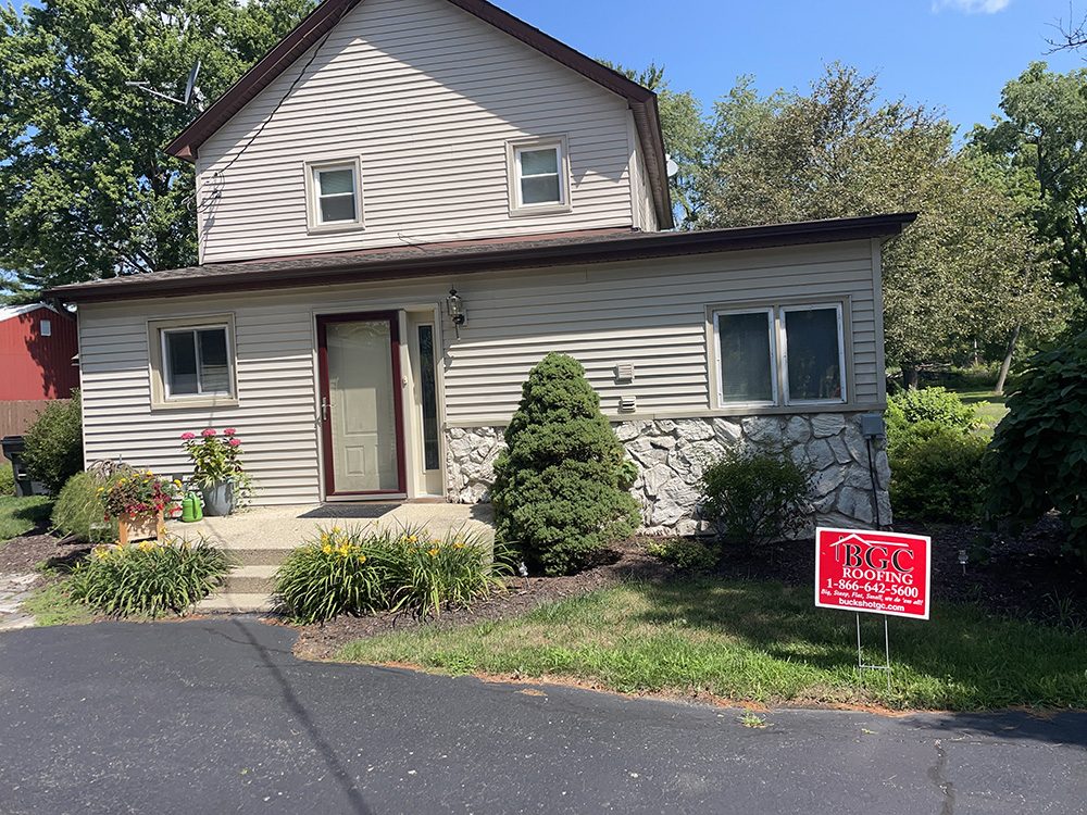 A well-maintained home with siding and a visible roofing sign in the front yard