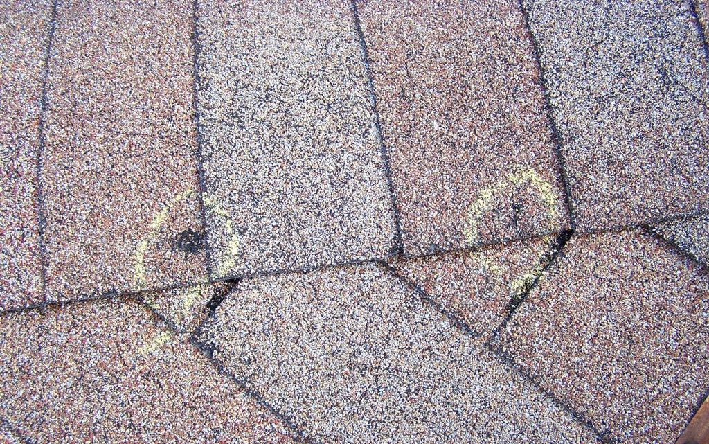Close-up view of asphalt shingles with chalk markings indicating damage
