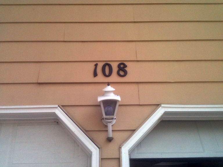 A close-up view of a house number and light fixture on a siding wall